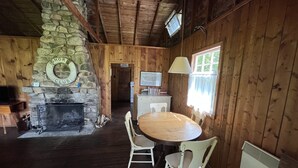 A rustic cabin interior with a stone fireplace, wooden walls, a dining table with chairs, and a television mounted on the wall. - Log Cabin #1 - Hubbards Beach (Hubbards)