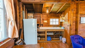 A wooden cabin interior with a kitchen area, including a refrigerator, sink, and wooden shelves. - Orchard Cabin #4 - Hubbards Beach (Hubbards)