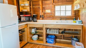 A compact kitchen with wooden walls, a white refrigerator, a microwave, a coffee maker, and a sink. - Orchard Cabin #4 - Hubbards Beach (Hubbards)