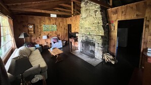 Een gezellig cabin interieur met een stenen open haard, houten wanden, een bank en een kleine tafel.