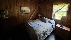 Een slaapkamer met een bed, een nachtkastje, een lamp, een foto aan de muur en een raam met gordijnen.