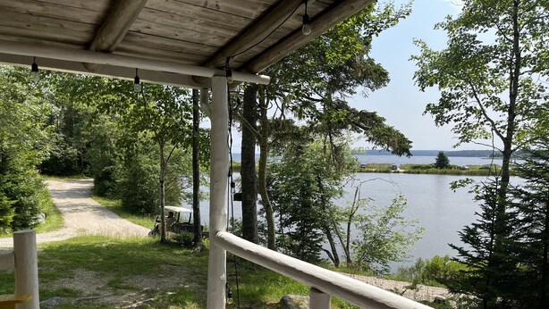 Une terrasse en bois dotée d’une rambarde, qui offre une vue sur un lac, et qui est entourée d’arbres. Un sentier mène de la terrasse à un endroit où l’on peut garer un véhicule.