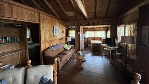 L’intérieur chaleureux d’un chalet avec un plancher en bois, un canapé, une table à manger et un téléviseur.