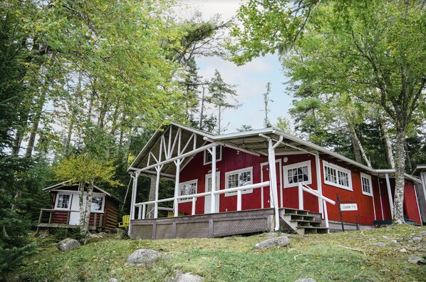 A red cabin with a porch and a small adjacent structure, surrounded by trees. - Beach Cottage - Silver Birches - Hubbards Beach (Hubbards)