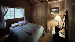 Une chambre dans un chalet en bois, avec un lit, une fenêtre avec des rideaux, une lampe et un tableau au mur.
