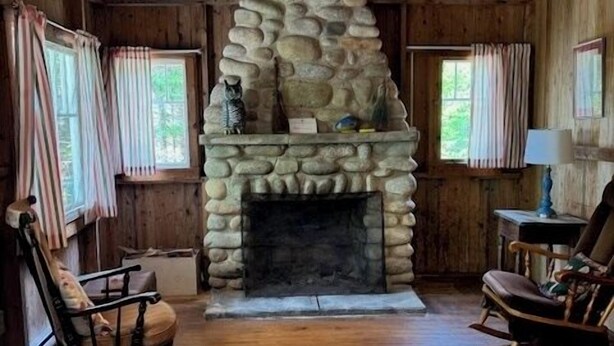 A rustic cabin interior with a stone fireplace, wooden floors, and two rocking chairs. - Beach Cottage - Whispering Firs - Hubbards Beach (Hubbards)