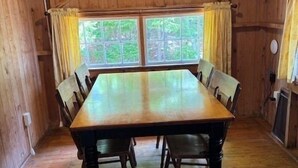 A wooden dining room with a large table and chairs, a window with curtains, and a wooden ceiling. - Beach Cottage - Whispering Firs - Hubbards Beach (Hubbards)