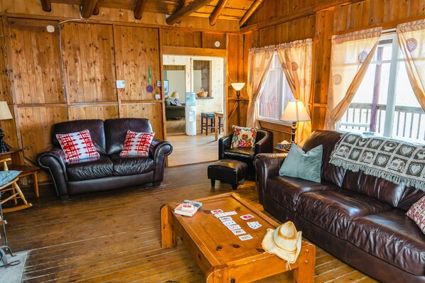 Ein gemütliches Blockhaus-Interieur mit Holzwänden, Ledersofas, einem Holztisch und Blick ins Freie.