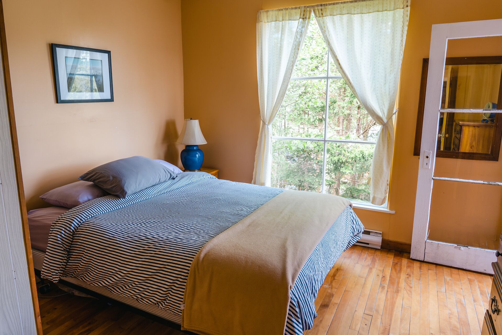 A bedroom with a bed, a nightstand, a lamp, a window with curtains, and a door.