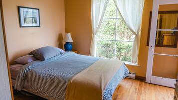 A bedroom with a bed, a nightstand, a lamp, a window with curtains, and a door.