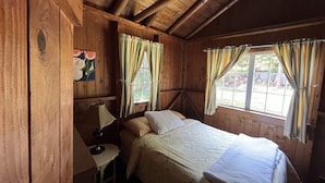 Ein Zimmer in einer Holzhütte mit einem Bett, einem Schreibtisch und zwei Fenstern mit Vorhängen.