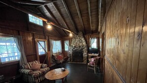Ein gemütliches Cabin-Interieur mit Kamin aus Stein, Holzwänden und einer komfortablen Sitzecke mit Sofa und Sesseln.