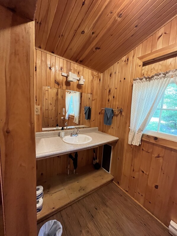 A wooden-paneled bathroom with a sink, mirror, and window. - Beach Cottage - Spruce Grove - Hubbards Beach (Hubbards)