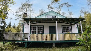 A small, single-story house with a green roof and white walls, featuring a porch with a wooden railing. - Beach Cottage - Pine Terrace - Hubbards Beach (Hubbards)