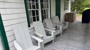 A covered porch with white Adirondack chairs and a wooden deck. - Beach Cottage - Pine Terrace - Hubbards Beach (Hubbards)