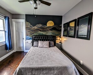 Un dormitorio con una cama grande, un ventilador de techo, un mural en la pared y una ventana con cortinas.