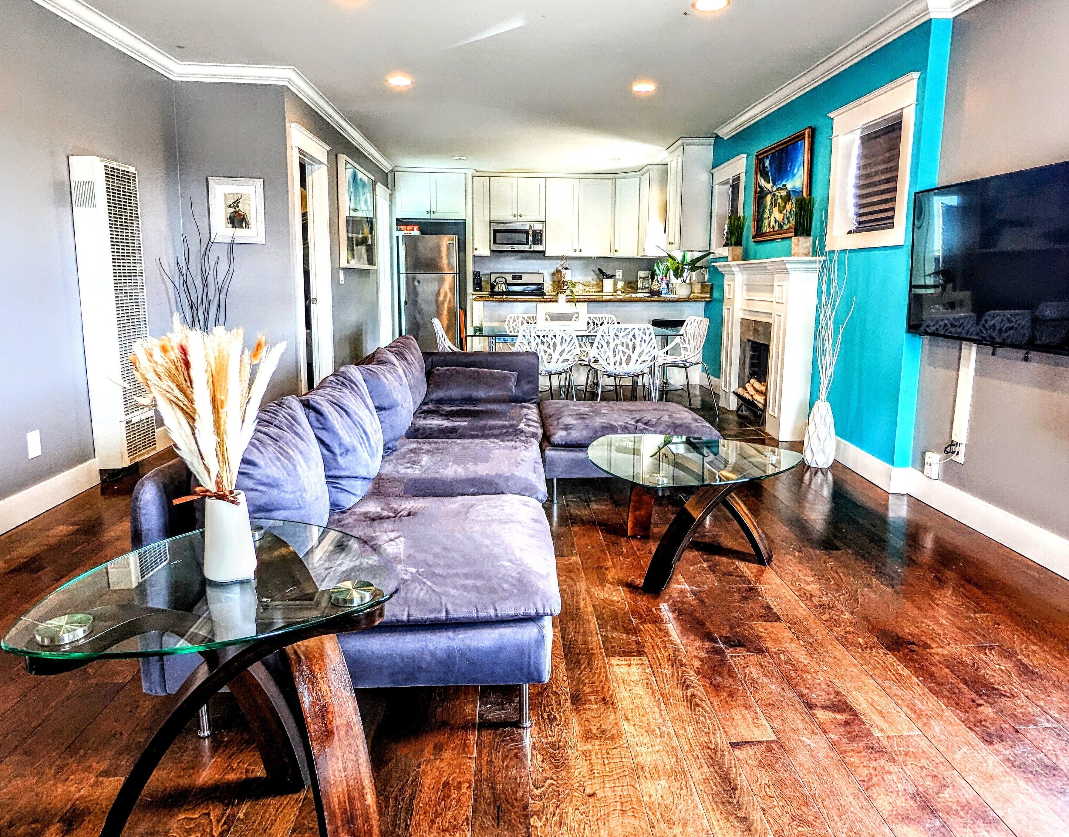 A modern living room with a sectional sofa, glass coffee table, and a dining area with a white table and chairs.