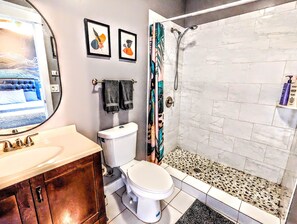 Un baño con inodoro, lavabo y ducha. Hay dos cuadros enmarcados en la pared.