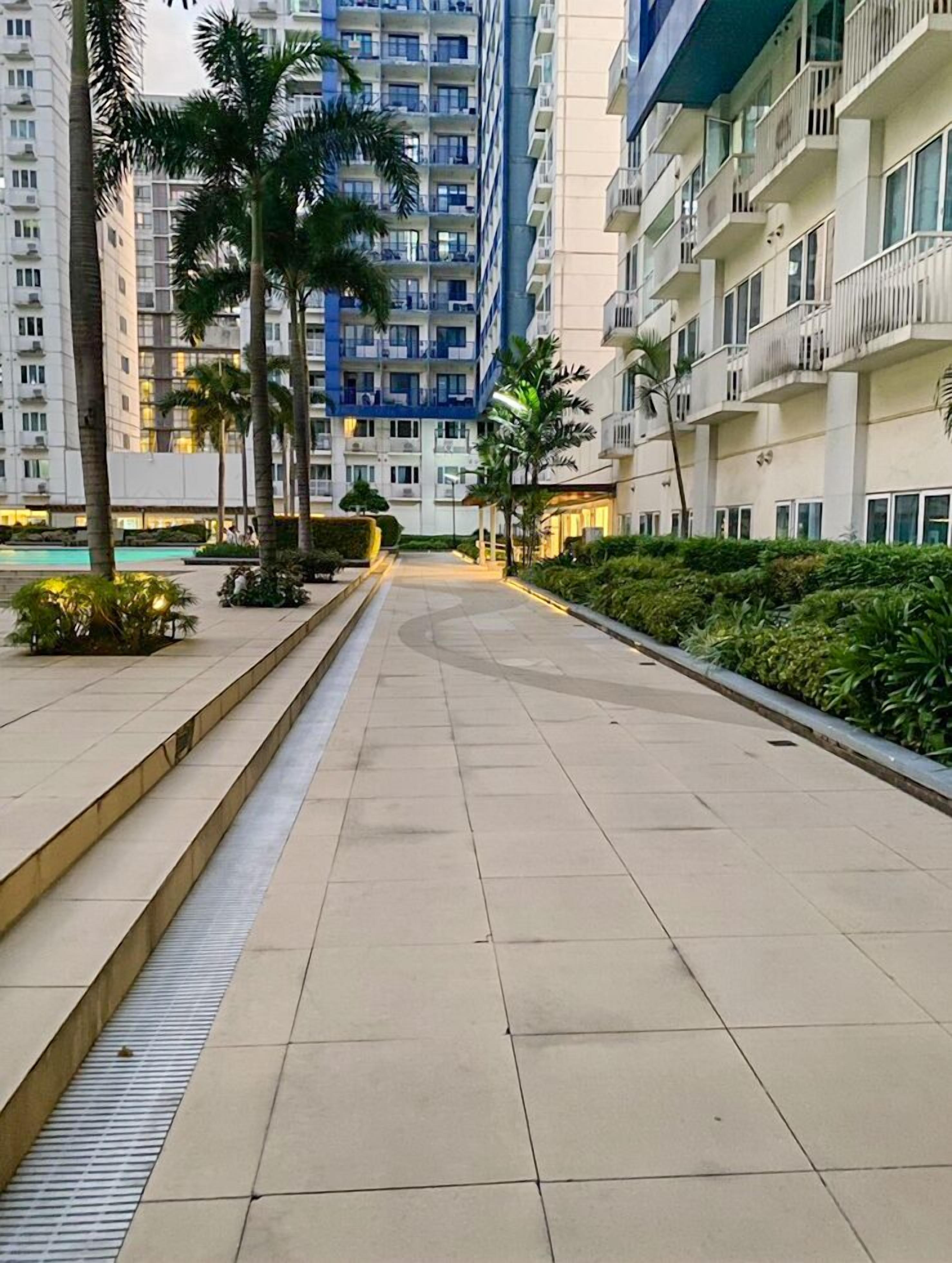 A modern residential building with multiple balconies, a central courtyard with palm trees, and a pool area.