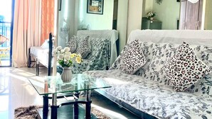 A modern living room with a glass coffee table, patterned sofa, and a large mirror. - Madison Place at Sea Residences powered by Cocotel (Pasay)