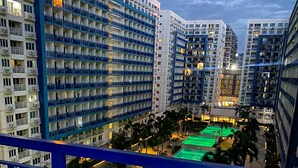A high-rise hotel with multiple balconies, a rooftop pool area, and a well-lit urban environment. - Madison Place at Sea Residences powered by Cocotel (Pasay)