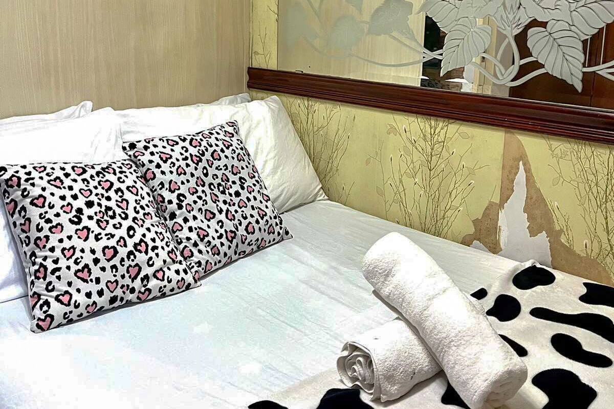 A hotel room with a bed, a leopard print pillow, a cow print blanket, and a mirror with a floral design.