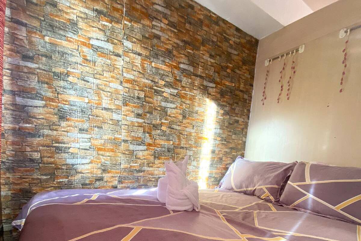 A room with a brick-patterned wall, two beds with patterned bedding, and a hanging light fixture.