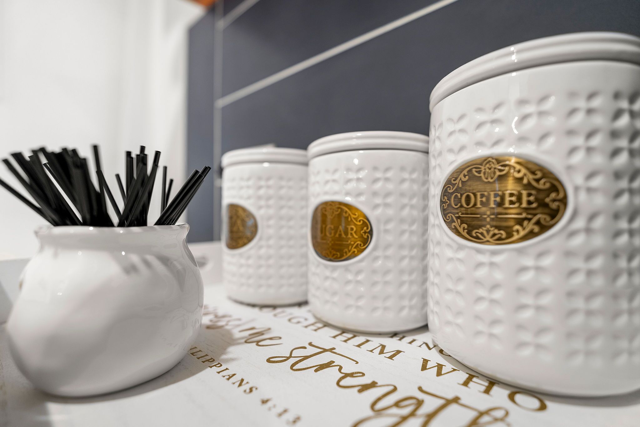 Drie witte keramische koffiemokken met reliëfpatronen en gouden accenten, geplaatst op een oppervlak met een decoratief lettertype.