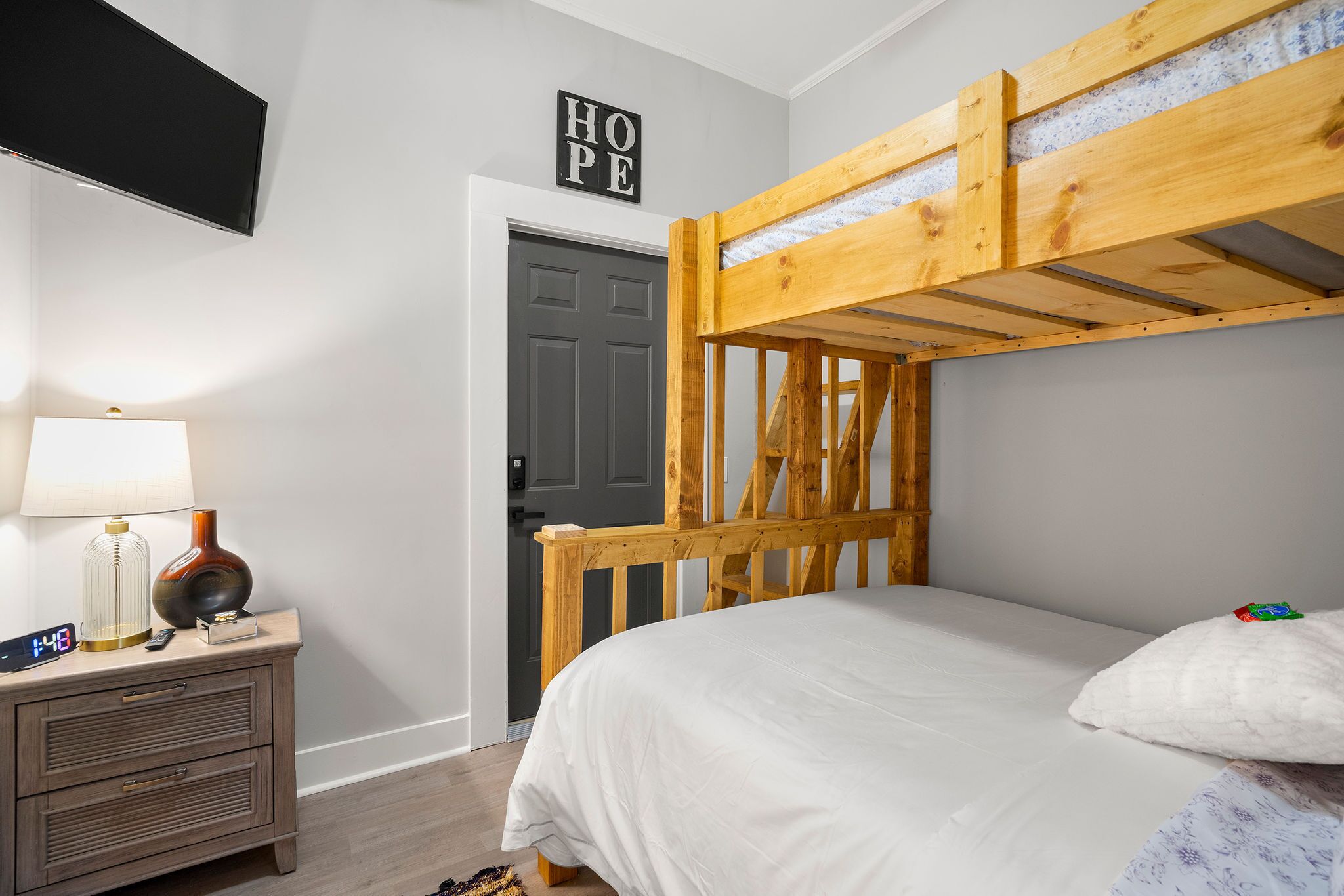 A bunk bed with a wooden headboard, a bedside table with a lamp, a clock, and a decorative item.