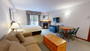 Una habitación de hotel con cama, sofá, mesa de centro de madera, chimenea, televisor y una mesa de comedor con sillas.