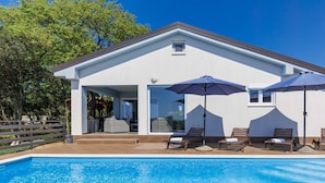 Ein modernes Haus mit Swimmingpool, Außenmöbeln und einer Pergola.