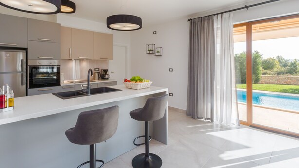 Une cuisine moderne dotée d’un grand îlot central, de tabourets de bar et offrant une vue sur une piscine.