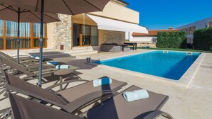 Un espace aménagé au bord de la piscine, avec des chaises longues, des parasols et un bâtiment en pierre en arrière-plan.