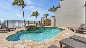 A pool area with lounge chairs, palm trees, and a view of the ocean. - 3134 Gulf-Front 5BR: Pool, Spa, Stunning Views (Fort Myers Beach)