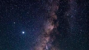 Una persona de pie bajo un cielo estrellado con una formación rocosa destacada.