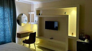 Una habitación de hotel moderna con una cama, un escritorio, una silla, un televisor montado en la pared y un pequeño estante con adornos.
