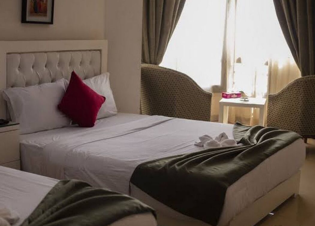 Habitación de hotel con dos camas, una mesita y un ventanal con cortinas.