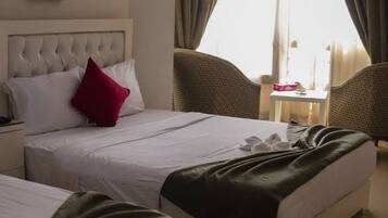Habitación de hotel con dos camas, una mesita y un ventanal con cortinas.