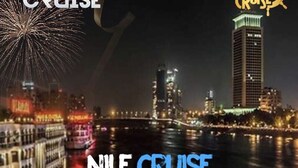 Un paisaje urbano nocturno con edificios iluminados y un crucero amarrado en la costa.