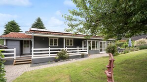 Ein zweistöckiges Haus mit weißem Zaun, einem Ziegeldach und einem Garten mit einem Hydranten.