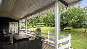 Ein überdachter Außenbereich mit Korbmöbeln, einem weißen Zaun und Blick auf einen gepflegten Garten.
