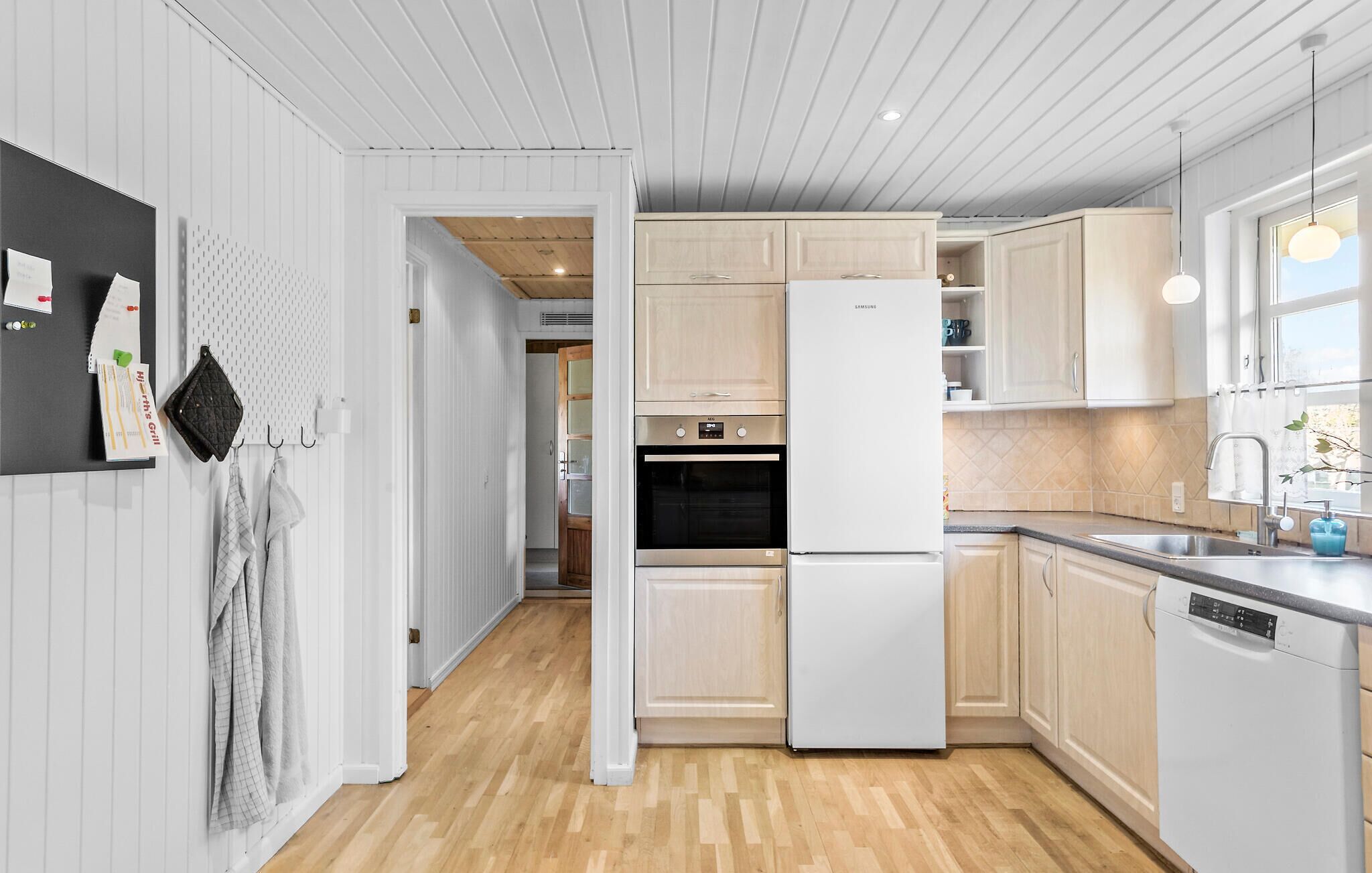 Una cocina moderna con armarios de madera clara, un refrigerador blanco y piso de madera.