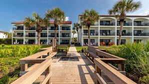 A resort with a wooden boardwalk leading to a building with multiple balconies and palm trees. - Palms of Seagrove D5 -Private Beach Access, Bikes, Pool & 5 Min to Seaside (Seagrove Beach)