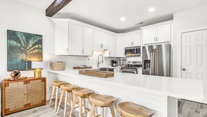 A modern kitchen with white cabinetry, stainless steel appliances, and a wooden bar stool area. - Palms of Seagrove D5 -Private Beach Access, Bikes, Pool & 5 Min to Seaside (Seagrove Beach)