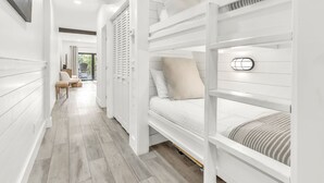 A modern, white-themed room with bunk beds, a wooden floor, and a view of the outdoors. - Palms of Seagrove D5 -Private Beach Access, Bikes, Pool & 5 Min to Seaside (Seagrove Beach)