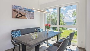 Un comedor moderno con una mesa de madera, sillas grises y un banco. Un cuadro de una escena de playa adorna la pared.