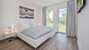 Un dormitorio moderno con una cama grande, una mesita de noche con lámpara, un cuadro en la pared y vistas por la ventana.