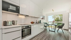 Una cocina moderna con armarios blancos, horno integrado, microondas y un comedor con mesa y sillas.