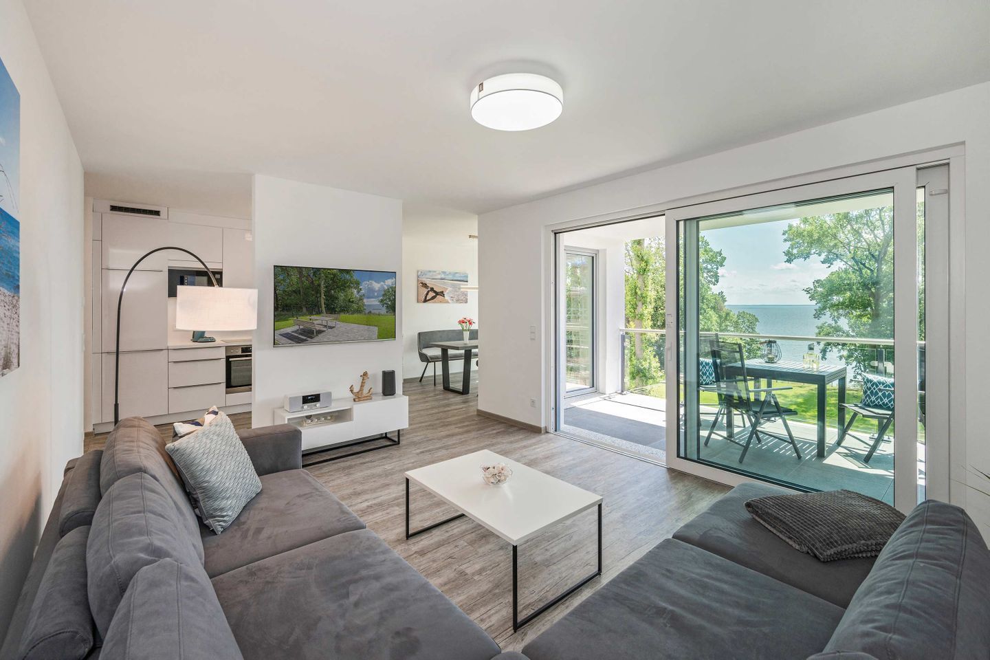 Ein modernes Wohnzimmer mit Sofa, Couchtisch, Fernseher und einem Balkon mit Blick.
