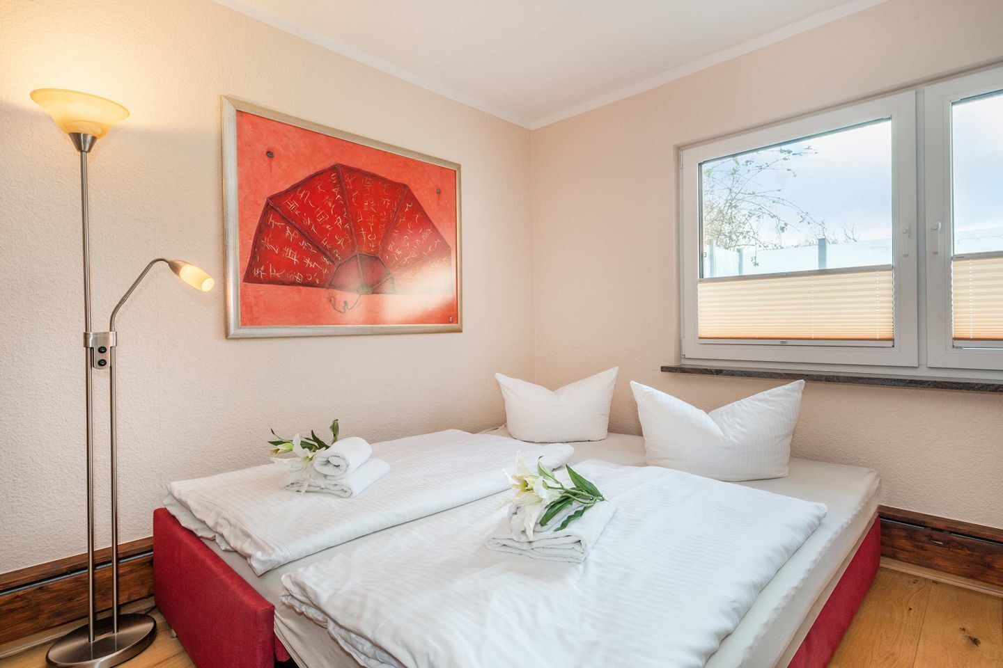 Une chambre d’hôtel avec deux lits, une lampe sur pied, un tableau et une fenêtre avec des stores.